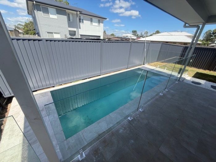 Compact backyard swimming pool with a glass pool fence