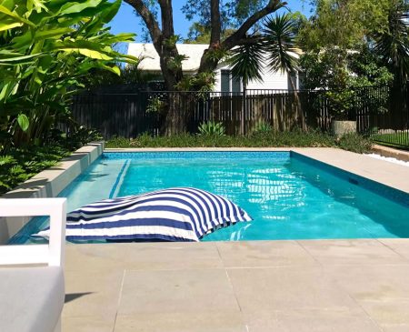 cannon-hill-swimming-pool-1 Beautiful aqua blue backyard swimming pool with a blue and white striped pool lounge, surrounded by lush green trees