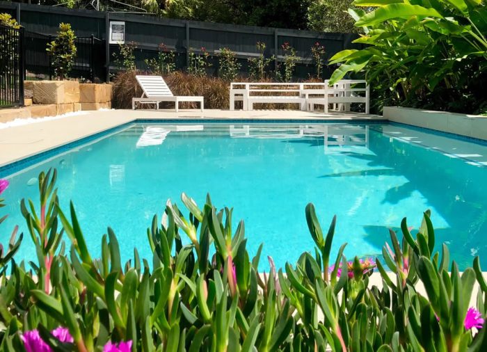 Beautiful aqua blue backyard swimming pool with lush green plants in the foreground